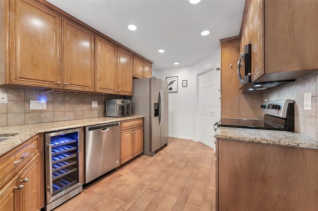 kitchen with appliances with stainless steel finishes, beverage cooler, baseboards, light wood-style floors, and recessed lighting