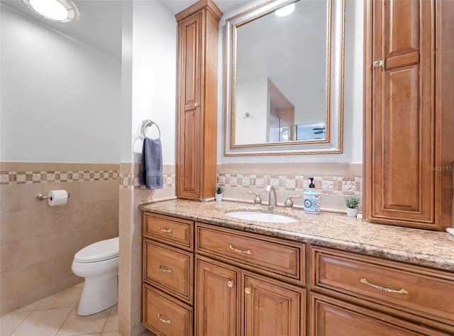 bathroom with toilet, vanity, a wainscoted wall, tile walls, and tile patterned flooring