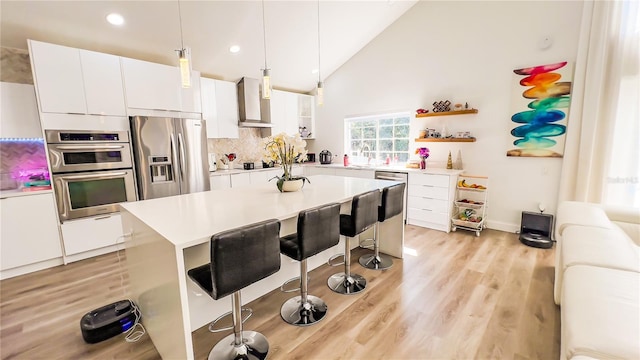 kitchen featuring wall chimney range hood, open shelves, a sink, stainless steel appliances, and a kitchen bar