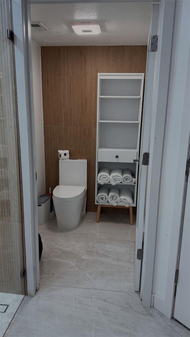bathroom featuring wood walls, toilet, and marble finish floor