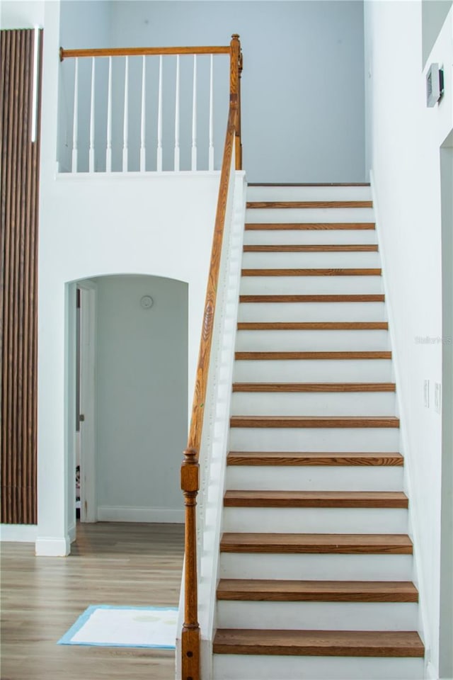 stairway with arched walkways, wood finished floors, and baseboards