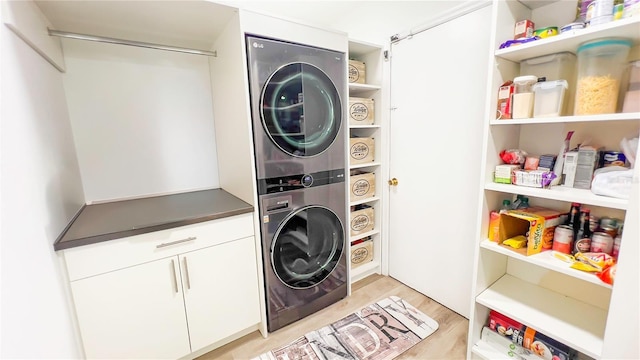 clothes washing area featuring stacked washer / drying machine, light wood-style flooring, and cabinet space