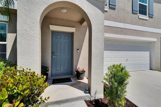 entrance to property featuring a garage, driveway, and stucco siding