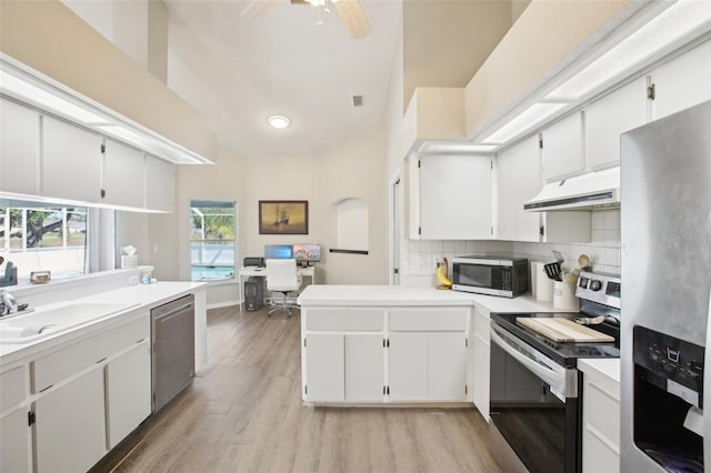 kitchen featuring under cabinet range hood, a sink, light wood-style floors, a peninsula, and appliances with stainless steel finishes