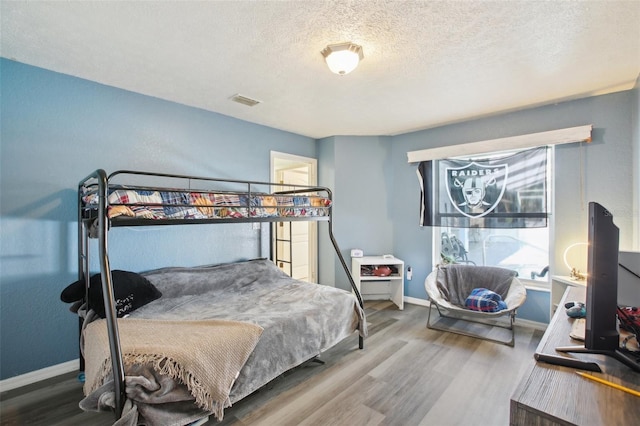 bedroom with wood finished floors, visible vents, and baseboards
