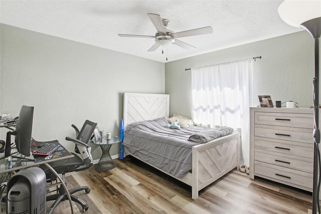 bedroom with a ceiling fan, baseboards, a textured wall, and wood finished floors