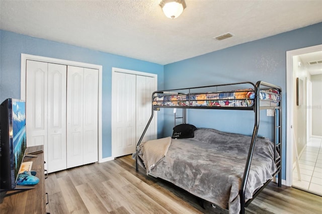 bedroom featuring two closets, visible vents, baseboards, and wood finished floors