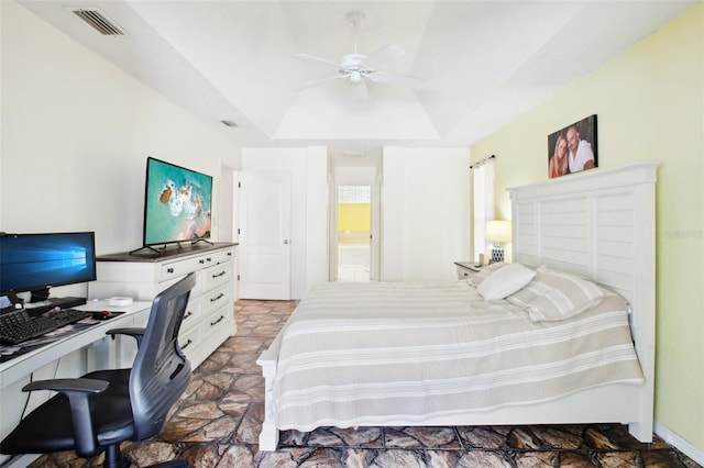 bedroom featuring a tray ceiling, stone finish floor, visible vents, and ceiling fan