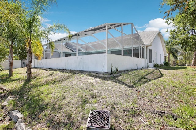 view of property exterior featuring glass enclosure, stucco siding, a lawn, and fence