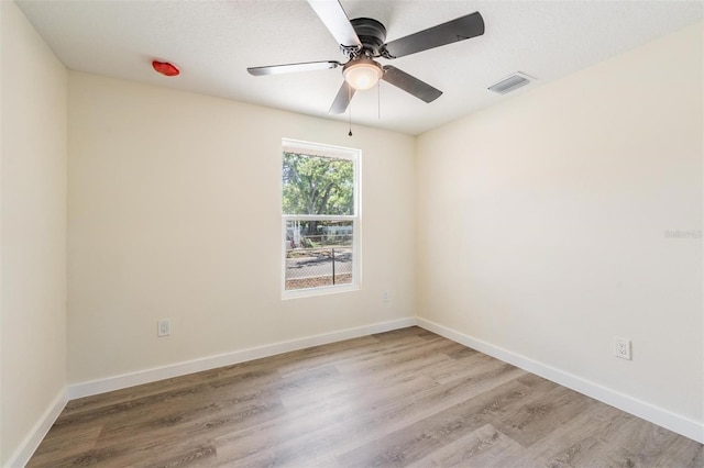 empty room with wood finished floors, baseboards, a ceiling fan, and visible vents
