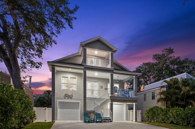 coastal home with covered porch, a garage, stairway, concrete driveway, and stucco siding