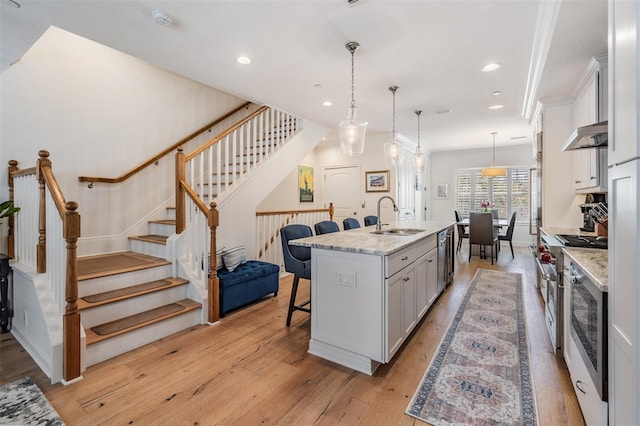 409 Regent Ln N, Saint Petersburg, FL 33701 - kitchen with a kitchen bar, light wood-type flooring, under cabinet range hood, a sink, and stainless steel appliances