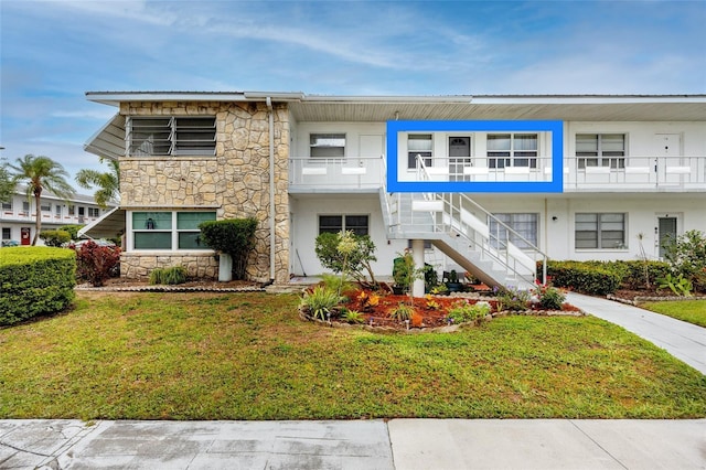 multi unit property featuring a front lawn, stucco siding, stone siding, and stairs