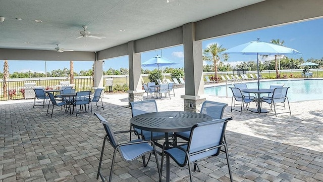 view of patio / terrace featuring outdoor dining space, a community pool, fence, and a ceiling fan