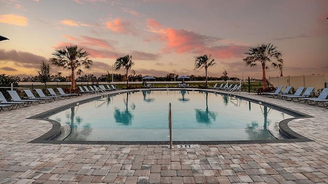 pool at dusk featuring a community pool, a patio area, and fence