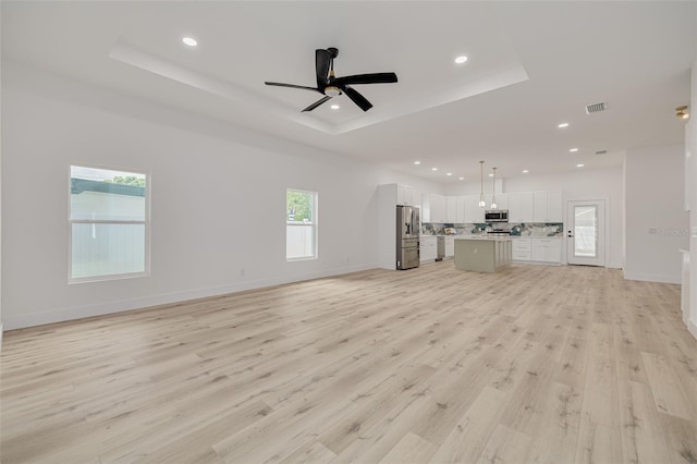 unfurnished living room featuring light wood finished floors, visible vents, recessed lighting, and a tray ceiling