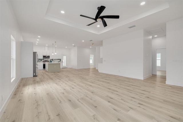 unfurnished living room with light wood-style flooring, visible vents, ceiling fan, a tray ceiling, and recessed lighting