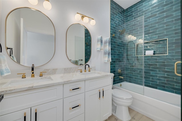bathroom with toilet, double vanity, a sink, and combined bath / shower with glass door