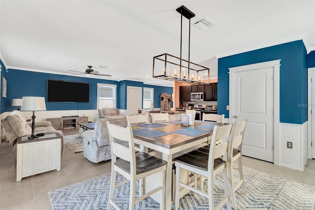 dining space with ceiling fan with notable chandelier, light tile patterned floors, wainscoting, and visible vents