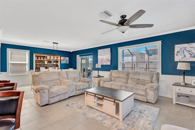 living area with visible vents, ornamental molding, ceiling fan, wainscoting, and light tile patterned flooring