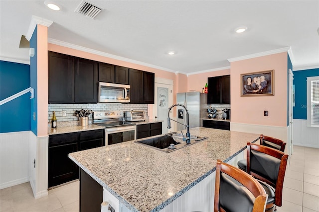 kitchen with visible vents, light tile patterned floors, a sink, appliances with stainless steel finishes, and an island with sink