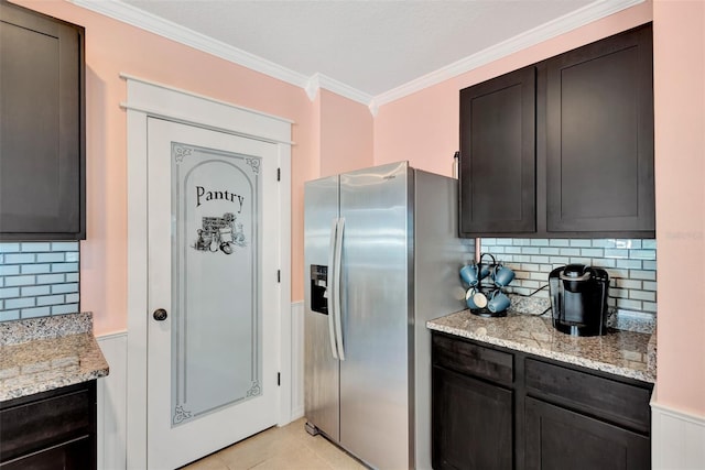 kitchen with crown molding, stainless steel fridge with ice dispenser, light tile patterned floors, a wainscoted wall, and light stone counters