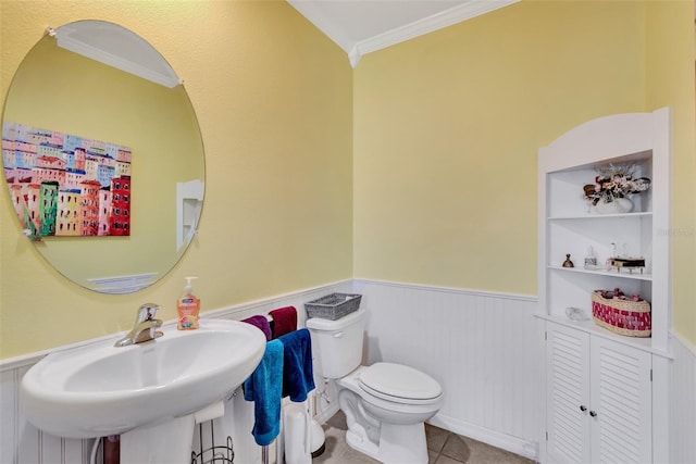 bathroom featuring ornamental molding, a wainscoted wall, toilet, a sink, and tile patterned floors