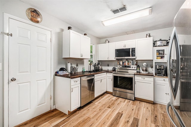 186 Grand Ave, Brooksville, FL 34604 - kitchen featuring stainless steel appliances, dark countertops, light wood-type flooring, and white cabinets