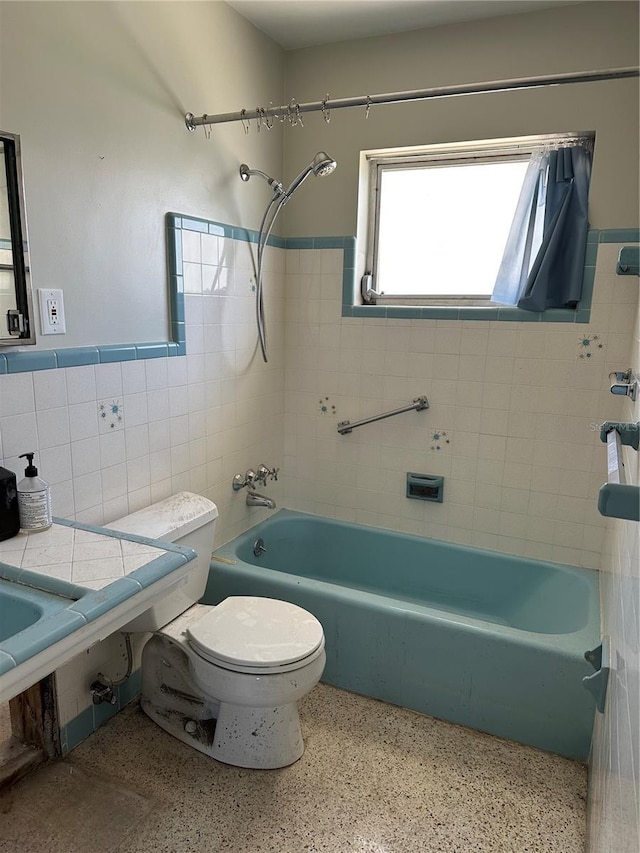 full bathroom with toilet, speckled floor,  shower combination, and tile walls