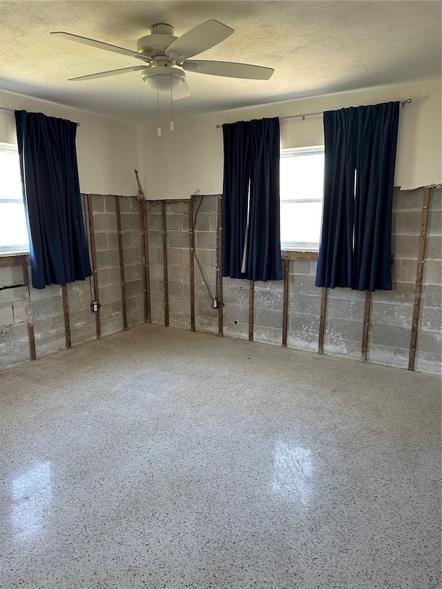 empty room with ceiling fan, speckled floor, and concrete block wall