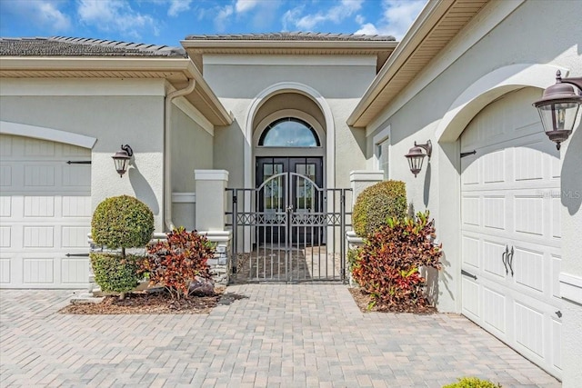 view of exterior entry with an attached garage, a gate, driveway, and stucco siding