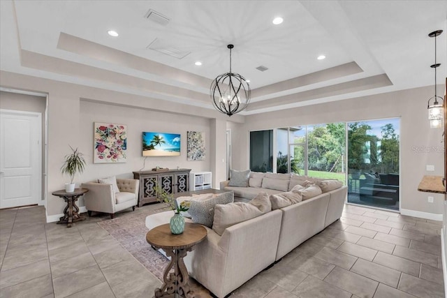 living room featuring a tray ceiling, baseboards, a chandelier, and visible vents
