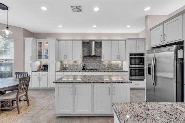 kitchen with visible vents, a center island, wall chimney exhaust hood, appliances with stainless steel finishes, and backsplash