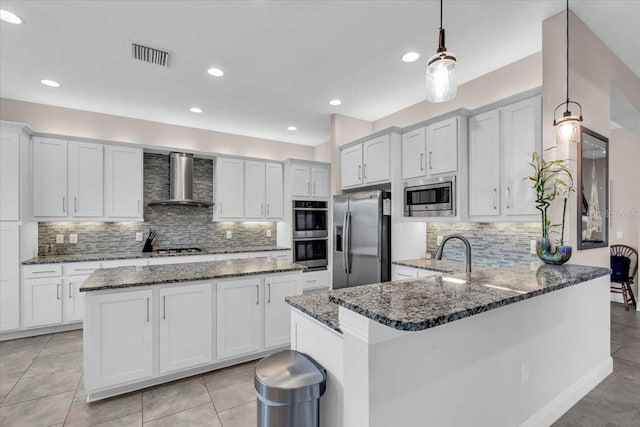 kitchen with wall chimney exhaust hood, appliances with stainless steel finishes, a peninsula, dark stone counters, and backsplash