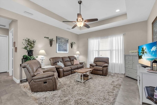 living room featuring visible vents, ceiling fan, a tray ceiling, and baseboards