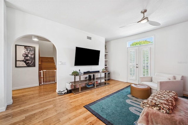 living area featuring stairs, visible vents, ceiling fan, arched walkways, and wood finished floors
