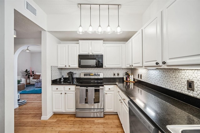 kitchen with arched walkways, appliances with stainless steel finishes, dark countertops, and white cabinets