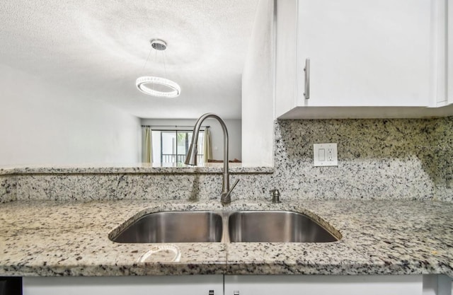 interior details with decorative light fixtures, a sink, white cabinetry, decorative backsplash, and light stone counters