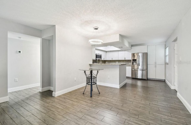 kitchen with a textured ceiling, a peninsula, white cabinets, wood finished floors, and stainless steel appliances