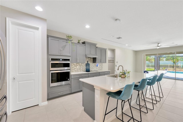 2511 Early Dawn Ct, Valrico, FL 33594 - kitchen with double oven, a kitchen breakfast bar, a sink, decorative backsplash, and gray cabinetry