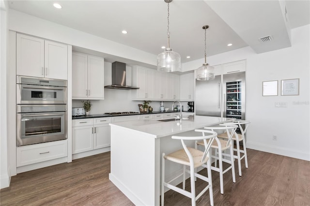 kitchen with dark wood-type flooring, visible vents, wall chimney exhaust hood, stainless steel appliances, and a sink