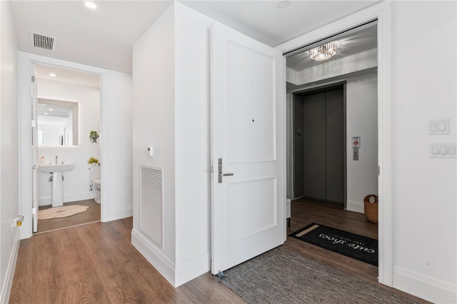 hall featuring wood finished floors, a notable chandelier, and visible vents