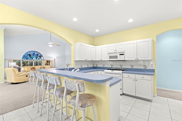 187 Sage Cir, Crystal Beach, FL 34681 - kitchen featuring white appliances, light colored carpet, arched walkways, a breakfast bar, and light tile patterned flooring
