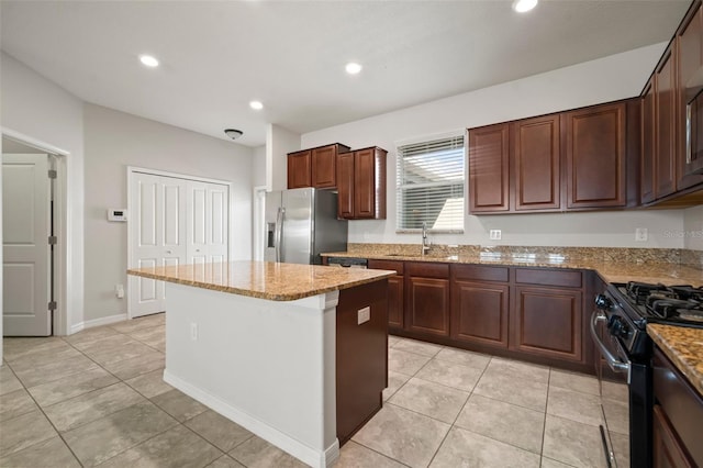 kitchen with a center island, stainless steel refrigerator with ice dispenser, gas range, a sink, and light stone counters