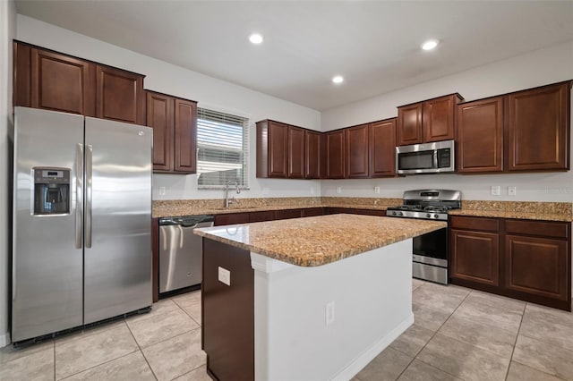 kitchen featuring a sink, appliances with stainless steel finishes, dark brown cabinetry, a kitchen island, and light stone counters