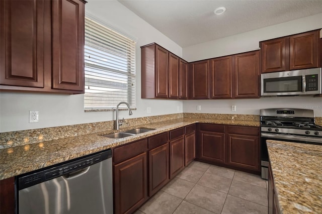 kitchen with a sink, light tile patterned flooring, dark stone counters, and stainless steel appliances