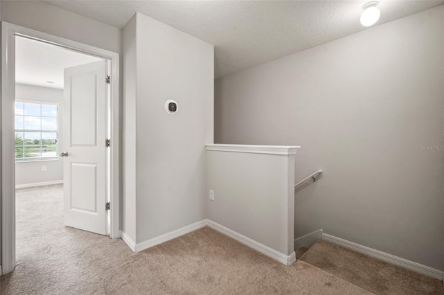 hallway featuring baseboards, an upstairs landing, and carpet floors