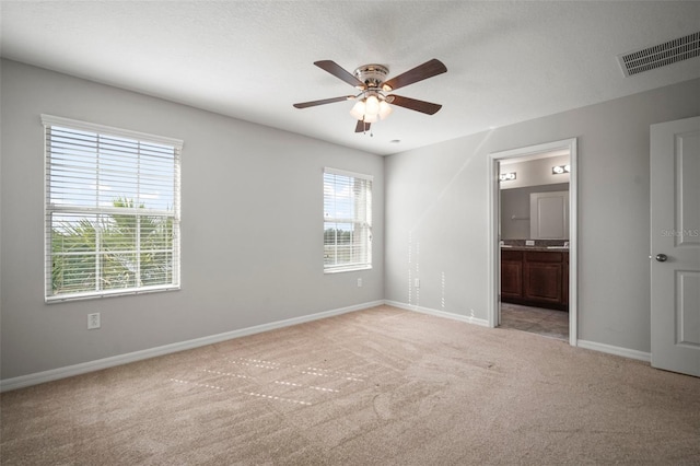 unfurnished bedroom with baseboards, ensuite bath, visible vents, ceiling fan, and light colored carpet