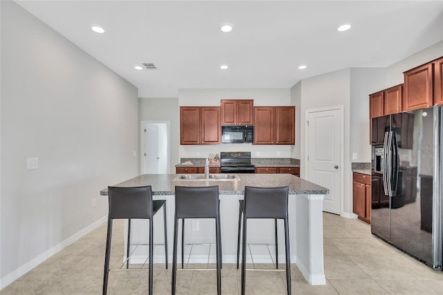 kitchen featuring black appliances, a kitchen island with sink, visible vents, a kitchen bar, and a sink