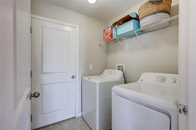 clothes washing area featuring laundry area, washing machine and clothes dryer, light tile patterned floors, and a textured ceiling